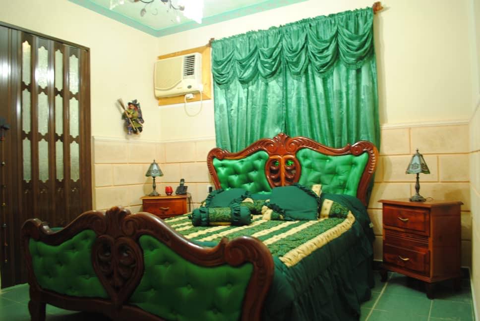 Room with a carved mahogany bed and bright emerald-green tufted headboard