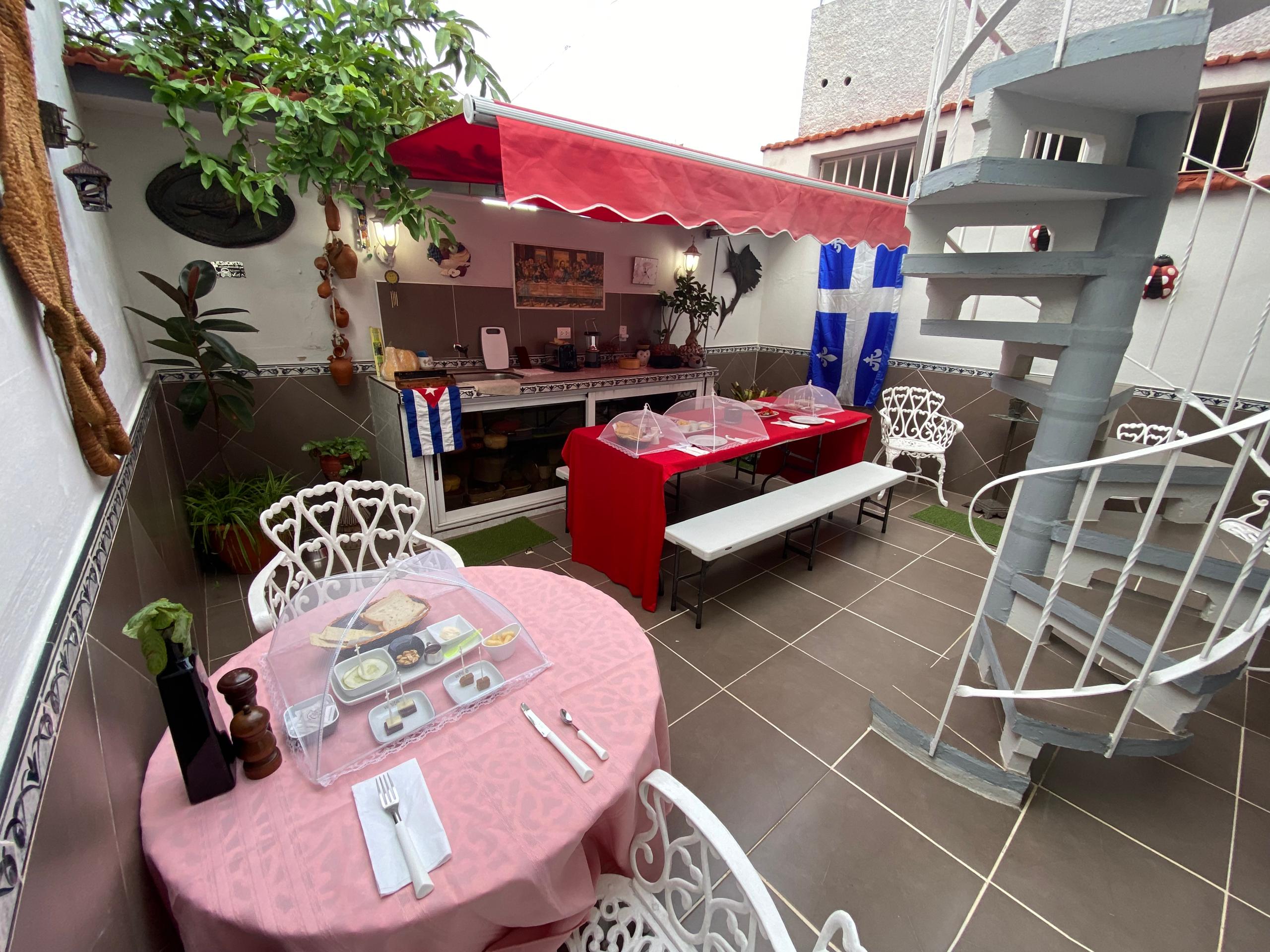 Sun terrace under a red awning, long red-clothed table, spiral staircase and potted plants