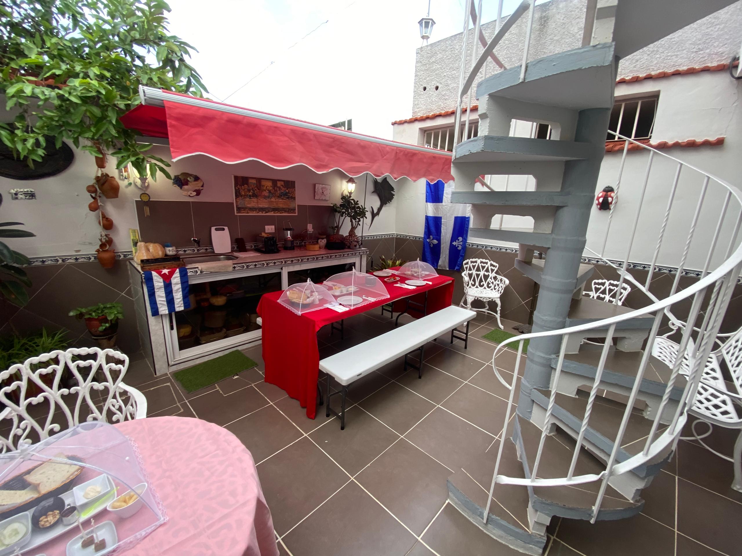 Daytime terrace with a red table set for breakfast, spiral staircase and lush plants