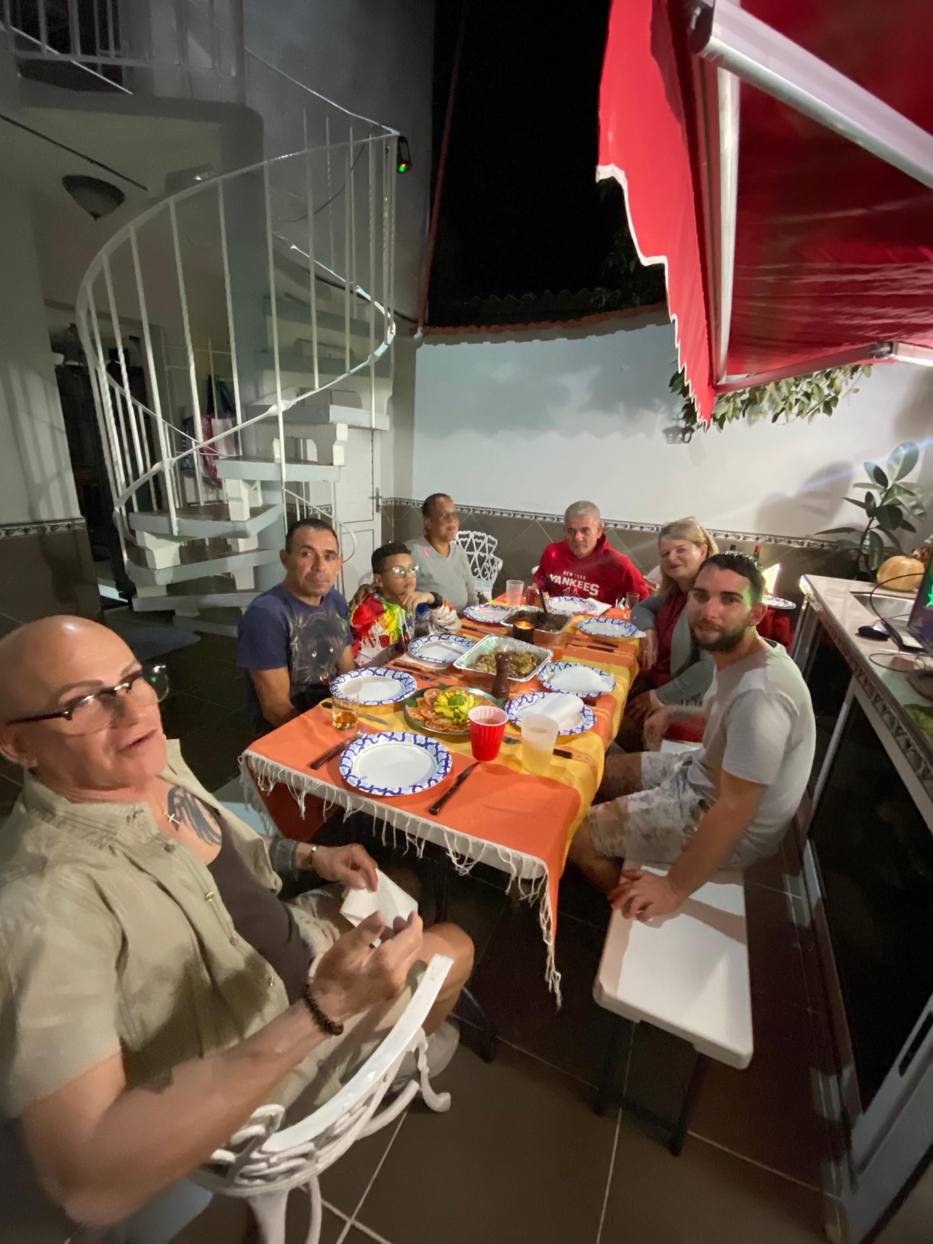 Group dinner on the terrace at night, spiral staircase visible, plates set on a yellow tablecloth