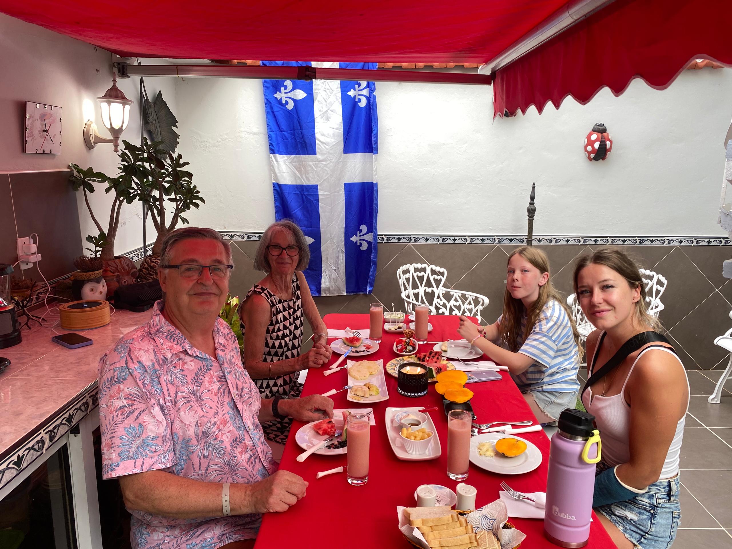 The same Quebec family, closer frame, smiling at the camera over breakfast plates