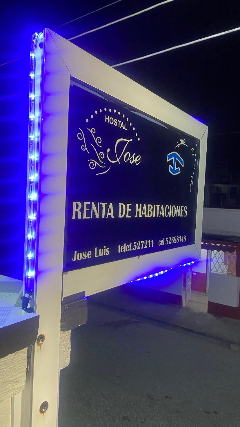 The Hostal Jose neon-lit sign at night with phone numbers in script